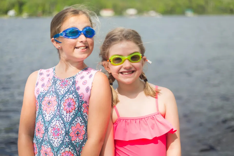 Dos niñas con goggles sonriendo junto al agua